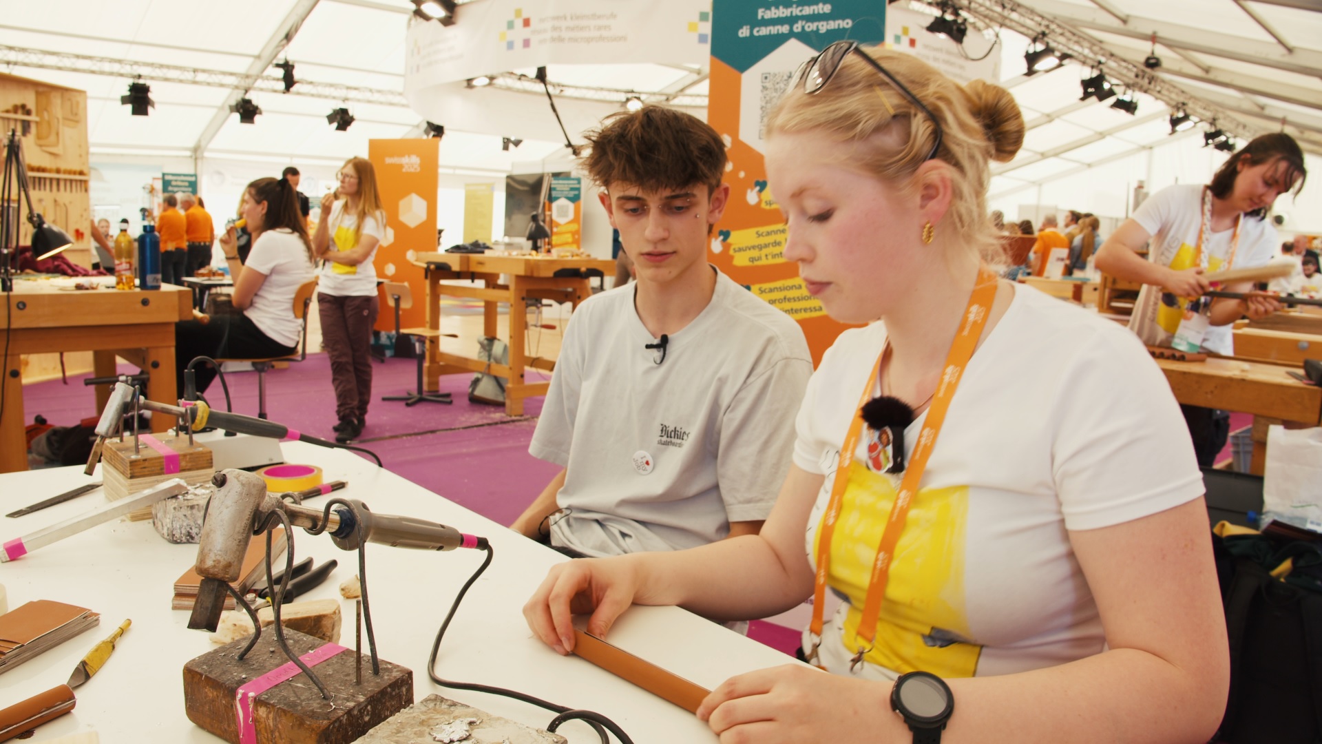 Zwei Jugendliche sitzen an einer Werkbankt mit einem grossen Lötkolben